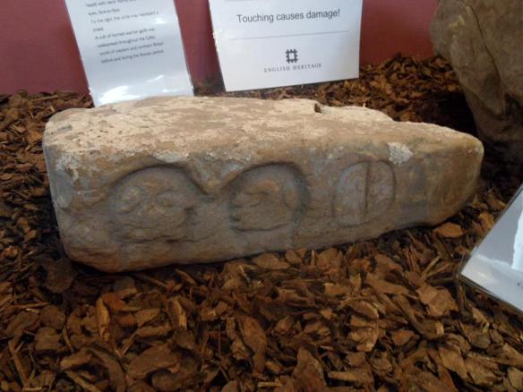 Stone on display at Wall museum, featuring two carved heads and what's thought to be a shield.
